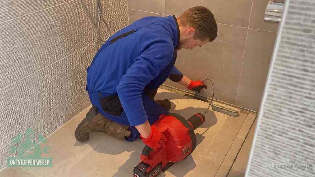 Een monteur ontstopt een langwerpige douchegoot met een elektrische veer, een doucheputje verstopt door haren en zeep in Weesp