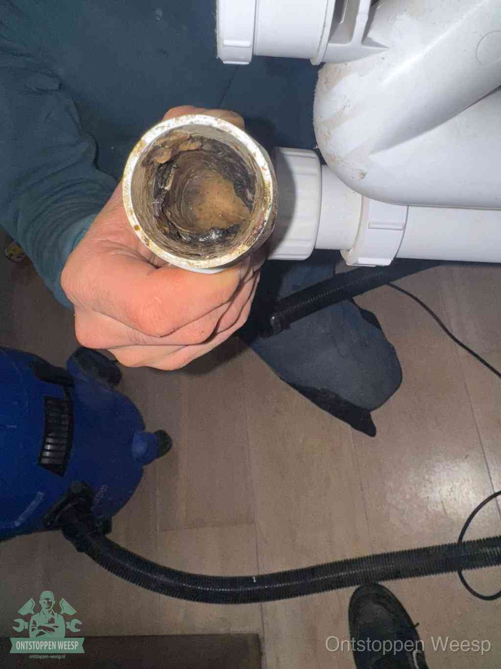 Een losgekoppeld PVC-afvoerbuisstuk dat van binnen volledig is dichtgeslibd met vet en vuil, de meest voorkomende oorzaak van verstoppingen in Weesp