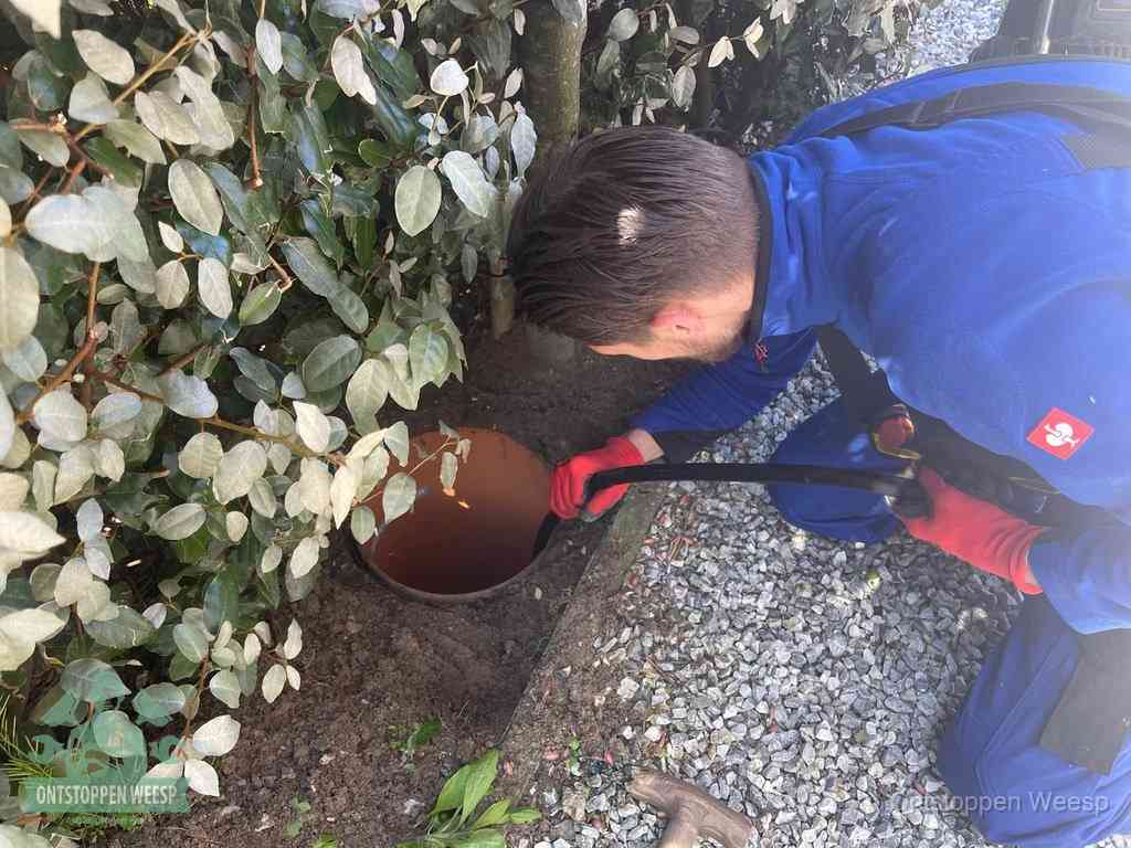 Een monteur voert een slang in een geopende rioolput in de tuin om het hoofdriool te ontstoppen in Weesp