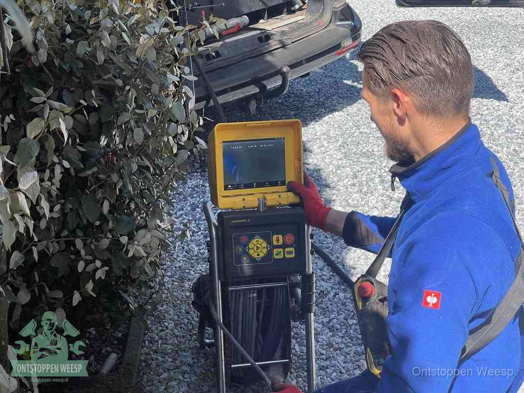 Een monteur bedient een rioolinspectiecamera met monitor en haspel om de verstopping in beeld te brengen in Weesp