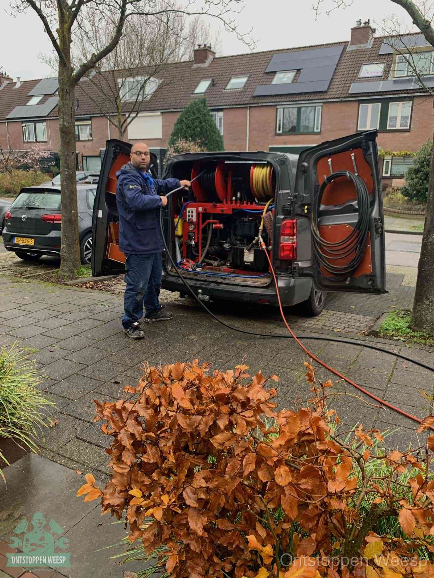 Een monteur staat bij zijn open bestelbus met hogedruk-rioolreinigingsapparatuur, klaar om binnen 30 minuten uit te rukken voor een spoedverstopping in Weesp