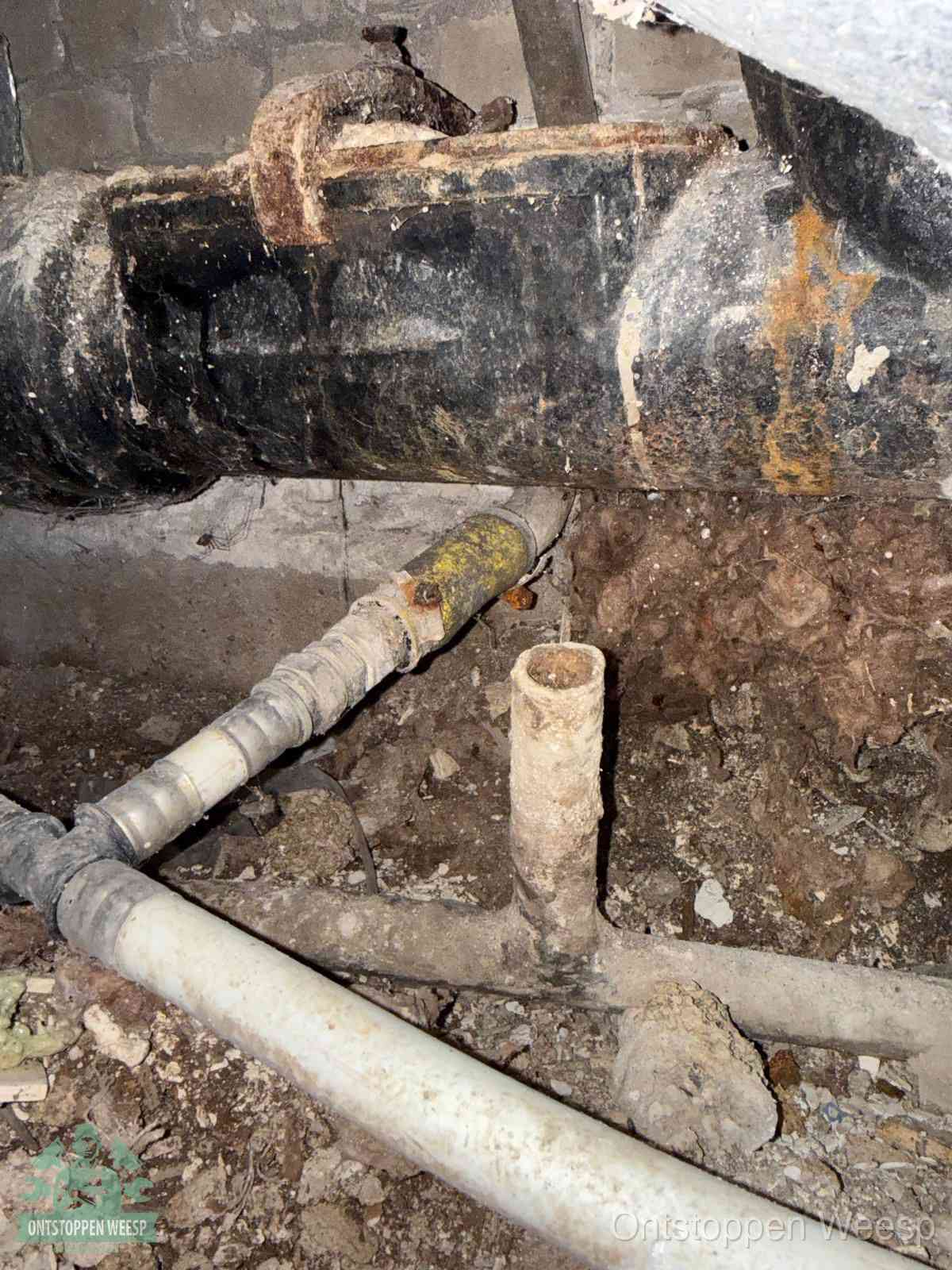 Een oude hoofdrioolbuis met roest- en kalkaanslag in een kruipruimte, oorzaak van terugkerende structurele rioolproblemen in Weesp