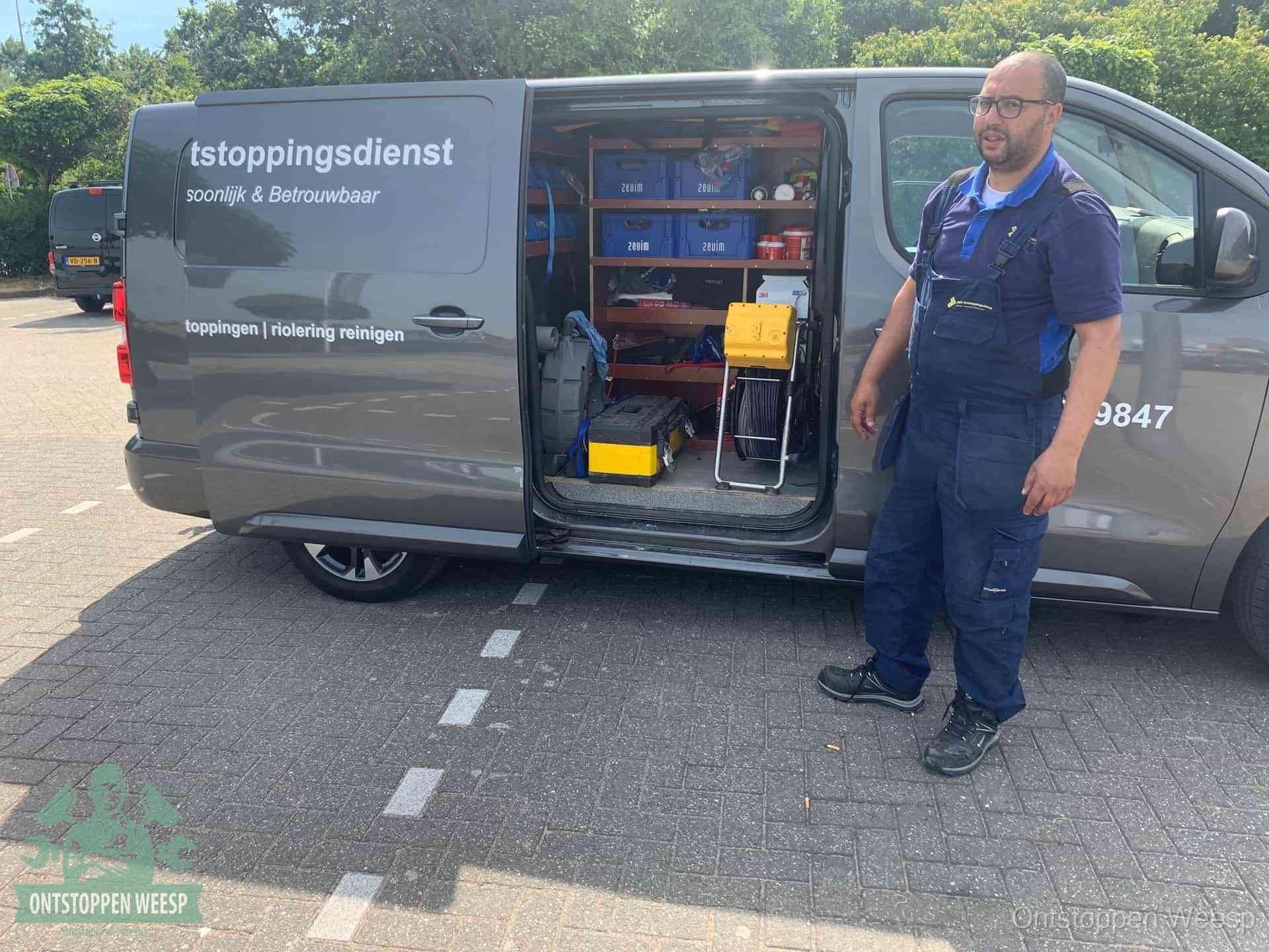 Een monteur staat klaar bij zijn bedrijfsbus met gereedschap, de vaste werkwijze van de ontstoppingsdienst in Weesp